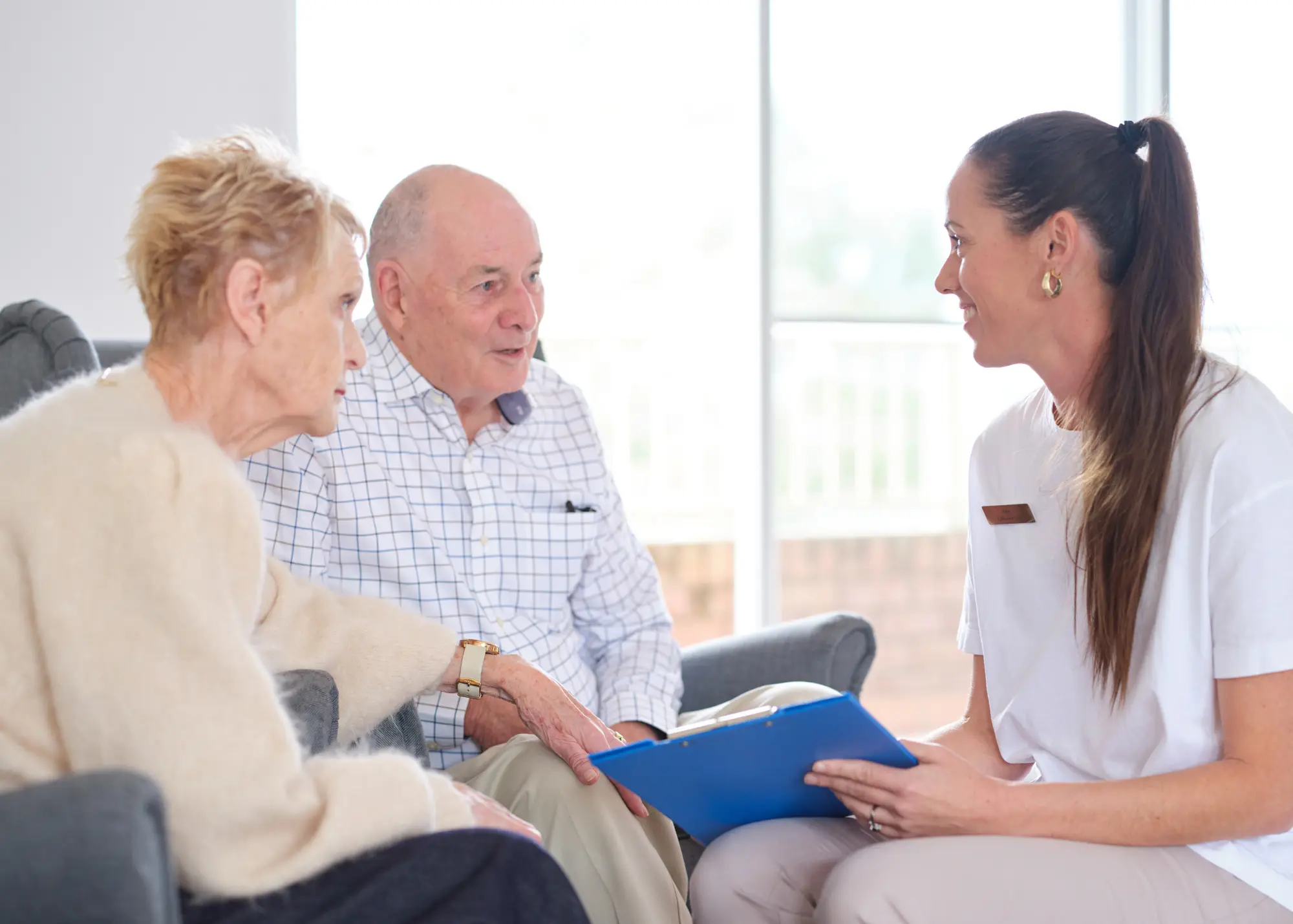 A care adviser with a clipboard talking through options with an older couple at home.